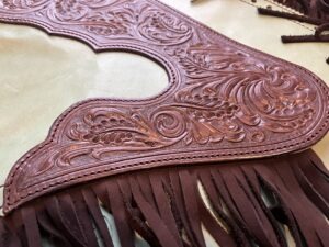 Auf diesem Bild ist die obere Passe von Westernchinks oder Chaps zu sehen. Das dunkelbraune Leder mit Ranken und Blättern im Westernstyle hebt sich deutlich vom Mintgrünen Haupt-Leder der Chinks ab.